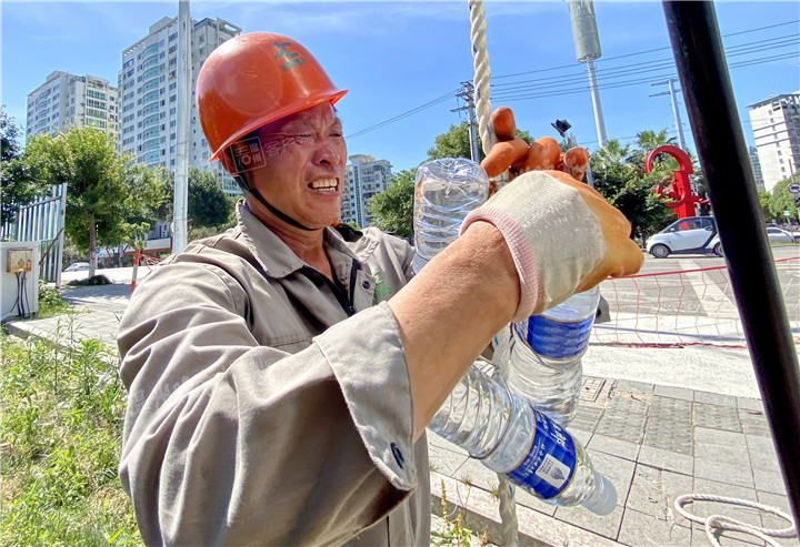 用绳子吊住矿泉水,送给高空作业的电力工人