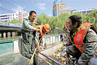 许永楠与在河面上清理垃圾的民兵交流工作.刘伟摄
